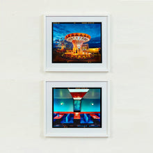 Load image into Gallery viewer, Two white framed photographs by Richard Heeps. The top photograph depicts a fairground ride, the chairoplanes, sits lit in golden and red colours against a dark blue sky. The bottom photograph is of a retro Wimpy in Norfolk. It has a retro diner vibe with dark blue seats and red tables against a blue wall.