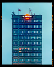 Load image into Gallery viewer, Photograph by Richard Heeps. High rise offices in a blue light with Martini logo on the top facade. 