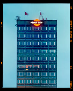 Photograph by Richard Heeps. High rise offices in a blue light with Martini logo on the top facade. 