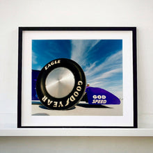 Load image into Gallery viewer, Black framed photograph by Richard Heeps. This photograph has the tyre and the very front tip of a drag car. The car&#39;s name is written on the front end &quot;God Speed&quot;. Behind the car are white vertical clouds shooting through a blue sky.