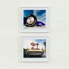 Load image into Gallery viewer, Two white framed photographs by Richard Heeps. The top photograph has the tyre and the very front tip of a drag car. The car&#39;s name is written on the front end &quot;God Speed&quot;. Behind the car are white vertical clouds shooting through a blue sky. The bottom photo features Las Vegas and has the back of a yellow chevy car and above the car sits the sign for the Stardust casino.