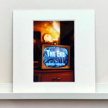 Load image into Gallery viewer, Mounted photograph by Richard Heeps. A retro small brown television sits on a wooden table displaying The End on a black and white film which shows as blue and white. In the background of the television is a warm light.