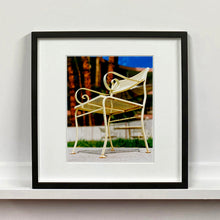 Load image into Gallery viewer, Black framed photograph by Richard Heeps. A cream chair sits on hard standing, in the back and slightly out of focus is lush green grass and warm red tree trunks.