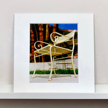 Load image into Gallery viewer, Mounted photograph by Richard Heeps. A cream chair sits on hard standing, behind the chair and slightly out of focus is lush green grass and warm red tree trunks.