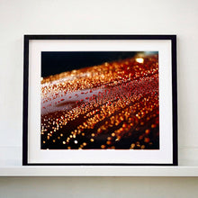 Load image into Gallery viewer, Black framed photograph by Richard Heeps. The photograph is of a brown metal surface with water droplets on. The lighting makes the droplets appear in different colours of orange and brown.
