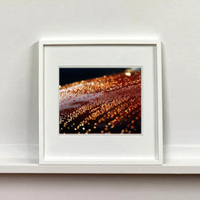 Load image into Gallery viewer, White framed photograph by Richard Heeps. The photograph is of a brown metal surface with water droplets on. The lighting makes the droplets appear in different colours of orange and brown.