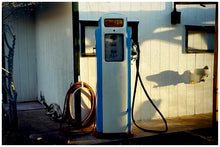 Load image into Gallery viewer, Photograph by Richard Heeps. A vintage petrol pump with a white front and blue sides, sitting outside a white slatted building.