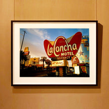 Load image into Gallery viewer, Black framed photograph by Richard Heeps. This photograph is of the outside of La Concha Motel. The gold flamboyant La Concha lettering is set on a big red background. Below the motel sign is NO VACANCY with just VACANCY lit in red, below this sits a sign for Budget rent a car. Other signs and palm trees are the background together with a blue sky.
