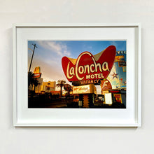 Load image into Gallery viewer, White framed photograph by Richard Heeps. This photograph is of the outside of La Concha Motel. The gold flamboyant La Concha lettering is set on a big red background. Below the motel sign is NO VACANCY with just VACANCY lit in red, below this sits a sign for Budget rent a car. Other signs and palm trees are the background together with a blue sky.