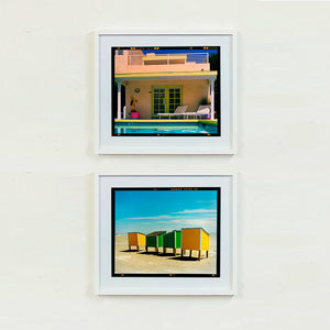 Two white framed photographs by Richard Heeps. The top photograph is of Palm Springs Pool Side and showcases classic mid-century Palm Springs California architecture. Cool blue skies and pool with accents of pink and almost neon yellow. The bottom photograph shows four beach lockers two green in the middle and two yellow on the outside on an empty beach.