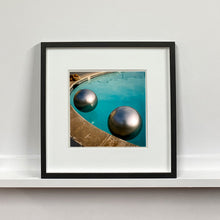 Load image into Gallery viewer, Black framed photograph by Richard Heeps. The corner of a circular swimming pool with two metallic silver beach balls floating on the water.