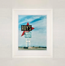 Load image into Gallery viewer, White framed photograph by Richard Heeps. A roadside sign on Route 66 in America. The word ROY&#39;S appears in a black sign with a big red arrow pointing to the left ground, below this VACANCY and on a green square the words MOTEL and CAFE.