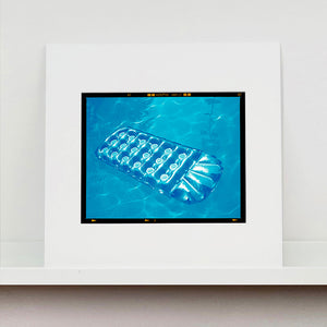 Mounted photograph by Richard Heeps. A transparent blue lilo is sun bathing on a blue pool. 