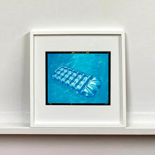 Load image into Gallery viewer, White framed photograph by Richard Heeps. A transparent blue lilo is sun bathing on a blue pool. 