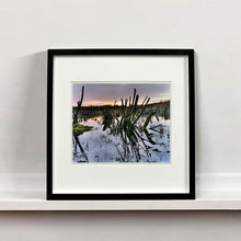 Load image into Gallery viewer, Black framed photograph by Richard Heeps. Photograph of cut down, lichen clad branches poking out of the flooded fen field. The branches are strikingly dark and create dark reflections with a golden sunset in the background.