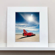 Load image into Gallery viewer, Mounted photograph by Richard Heeps. A red drag car with a 75 written on its fin sits on a salt plain the front facing away towards the right. A blue cloudy sky is overhead.