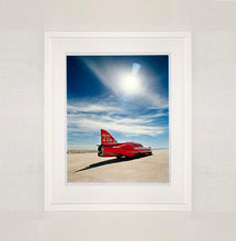 Load image into Gallery viewer, White framed photograph by Richard Heeps. A red drag car with a 75 written on its fin sits on a salt plain the front facing away towards the right. A blue cloudy sky is overhead.