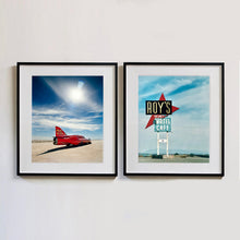 Load image into Gallery viewer, Two black framed photographs by Richard Heeps. The left hand side photograph is of a red drag car with a 75 written on its fin sits on a salt plain the front facing away towards the right. A blue cloudy sky is overhead. The photograph on the right hand side is a large sign for Roy&#39;s Motel and Cafe, on flat land with mountains in the background and a vast sky behind.. 