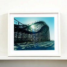Load image into Gallery viewer, White framed photograph by Richard Heeps. Great White Roller coaster sits empty on the beach in the setting sun.