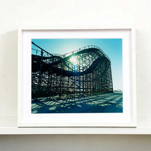 White framed photograph by Richard Heeps. Great White Roller coaster sits empty on the beach in the setting sun.