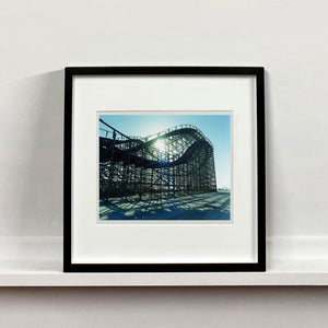 Black framed photograph by Richard Heeps. Great White Roller coaster sits empty on the beach in the setting sun.
