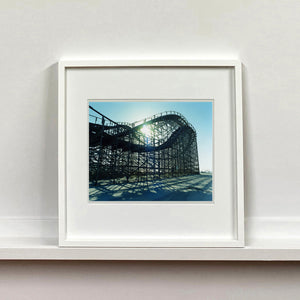 White framed photograph by Richard Heeps. Great White Roller coaster sits empty on the beach in the setting sun.