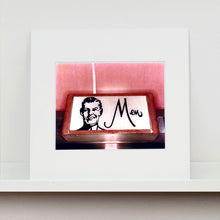 Load image into Gallery viewer, Mounted photograph by Richard Heeps. A kitsch Men&#39;s toilet sign. The sign has the word Men alongside an outline of 1950s man. The sign sits in a wooden frame and sits against a pink tiled wall.