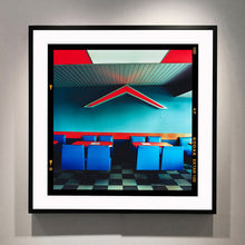 Load image into Gallery viewer, Black framed photograph by Richard Heeps. This photograph captures the inside of a Wimpy Restaurant in Norfolk. There is bright blue seats and red tables. The walls are blue and there is a big red chevron light attached to the wall. 