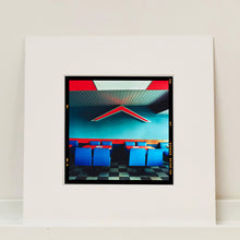 Load image into Gallery viewer, Mounted photograph by Richard Heeps. This photograph captures the inside of a Wimpy Restaurant in Norfolk. There is bright blue seats and red tables. The walls are blue and there is a big red chevron light attached to the wall. 