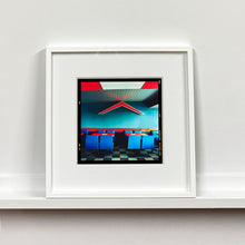 Load image into Gallery viewer, White framed photograph by Richard Heeps. This photograph captures the inside of a Wimpy Restaurant in Norfolk. There is bright blue seats and red tables. The walls are blue and there is a big red chevron light attached to the wall. 