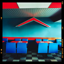 Load image into Gallery viewer, Photograph by Richard Heeps. This photograph captures the inside of a Wimpy Restaurant in Norfolk. There is bright blue seats and red tables. The walls are blue and there is a big red chevron light attached to the wall. 