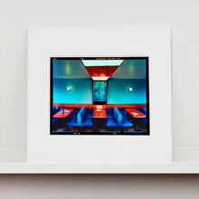 Load image into Gallery viewer, Mounted photograph by Richard Heeps. The inside of a Wimpy restaurant. Blue upholstered double seats pinned to the floor and separated by striking red tables. The walls are blue with a blue picture of trees with a black surround aligned with the middle table.