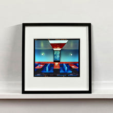 Load image into Gallery viewer, Black framed photograph by Richard Heeps. The inside of a Wimpy restaurant. Blue upholstered double seats pinned to the floor and separated by striking red tables. The walls are blue with a blue picture of trees with a black surround aligned with the middle table.