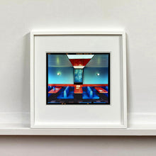 Load image into Gallery viewer, White framed photograph by Richard Heeps. The inside of a Wimpy restaurant. Blue upholstered double seats pinned to the floor and separated by striking red tables. The walls are blue with a blue picture of trees with a black surround aligned with the middle table.