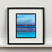 Load image into Gallery viewer, Black framed photograph by Richard Heeps. The blue bay at Llandudno, cut across the middle with path and railings with a gap right in the middle.