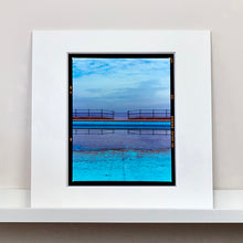 Load image into Gallery viewer, Mounted photograph by Richard Heeps. The blue bay at Llandudno, cut across the middle with path and railings with a gap right in the middle.