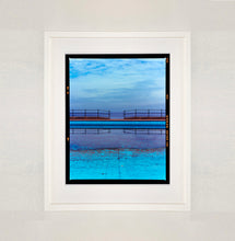 Load image into Gallery viewer, White framed photograph by Richard Heeps. The blue bay at Llandudno, cut across the middle with path and railings with a gap right in the middle.