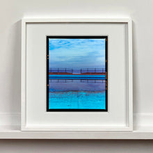Load image into Gallery viewer, White framed photograph by Richard Heeps. The blue bay at Llandudno, cut across the middle with path and railings with a gap right in the middle.