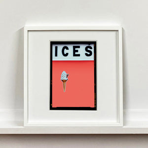 White framed photograph by Richard Heeps.  At the top black letters spell out ICES and below is depicted a 99 icecream cone sitting left of centre against a melondrama red orange coloured background.  