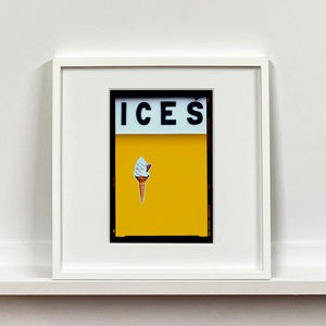 White framed photograph by Richard Heeps.  At the top black letters spell out ICES and below is depicted a 99 icecream cone sitting left of centre against a mustard yellow coloured background.  