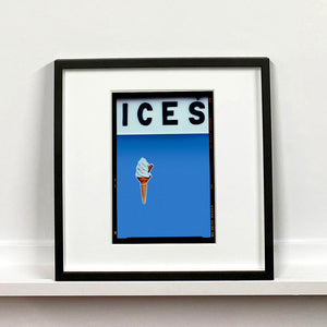 Black framed photograph by Richard Heeps.  At the top black letters spell out ICES and below is depicted a 99 icecream cone sitting left of centre against a baby blue coloured background.  