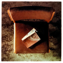Load image into Gallery viewer, Photograph by Richard Heeps. The photograph looks down on a brown padded side chair. On it sits a waterstained and battered brown covered Holy Bible.
