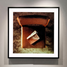 Load image into Gallery viewer, Black framed photograph by Richard Heeps. The photograph looks down on a brown padded side chair. On it sits a waterstained and battered brown covered Holy Bible.