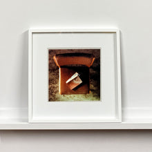 Load image into Gallery viewer, White framed photograph by Richard Heeps. The photograph looks down on a brown padded side chair. On it sits a waterstained and battered brown covered Holy Bible.