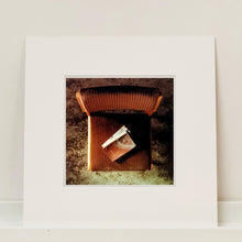 Load image into Gallery viewer, Mounted photograph by Richard Heeps. The photograph looks down on a brown padded side chair. On it sits a waterstained and battered brown covered Holy Bible.