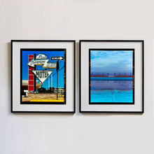 Load image into Gallery viewer, Two black framed photographs by Richard Heeps. On one side the photograph depicts a group of signs on an American Road. Arrow sign pointing to the left to Pink Champagne, pointing down with MOTEL and a one way sign pointing to the right. The Motel signs sit in front of the hotel on a red squared ladder. On the right hand side the photograph is an expanse of water of the most beautiful blues, the scene is cut in half by a blue concrete path, with a wooden and metal fence, with a gap in the middle.