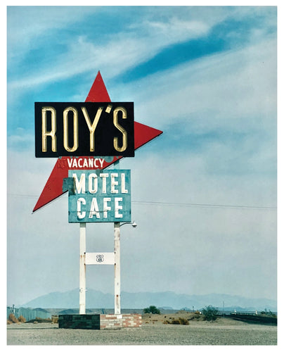Photograph by Richard Heeps. A roadside sign on Route 66 in America. The word ROY'S appears in a black sign with a big red arrow pointing to the left ground, below this VACANCY and on a green square the words MOTEL and CAFE.