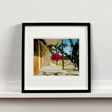 Load image into Gallery viewer, Black framed photograph held by photographer,Richard Heeps. A flowering bougainvillea hangs outside a motel entrance.