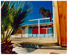 Load image into Gallery viewer, Photograph by Richard Heeps. A colourful but derelict vintage motel sits in the blue Californian sun. Palm trees appear behind and to the side. 