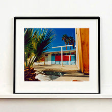 Load image into Gallery viewer, Black framed photograph by Richard Heeps. A colourful but derelict vintage motel sits in the blue Californian sun. Palm trees appear behind and to the side. 
